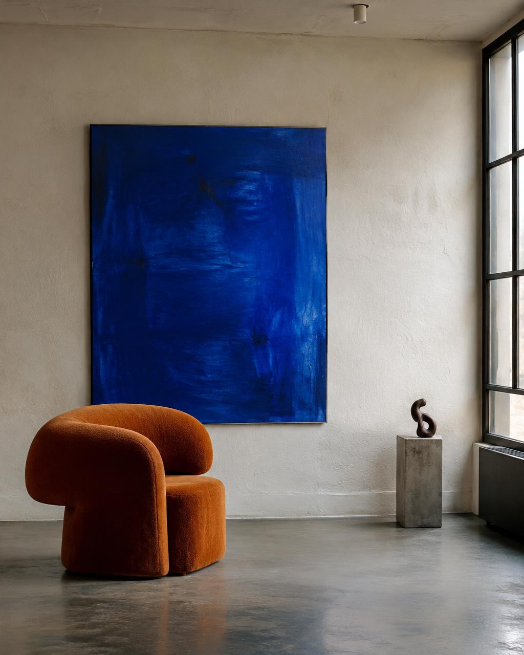 Plaster-walled room with a single sculptural orange chair and large cobalt painting